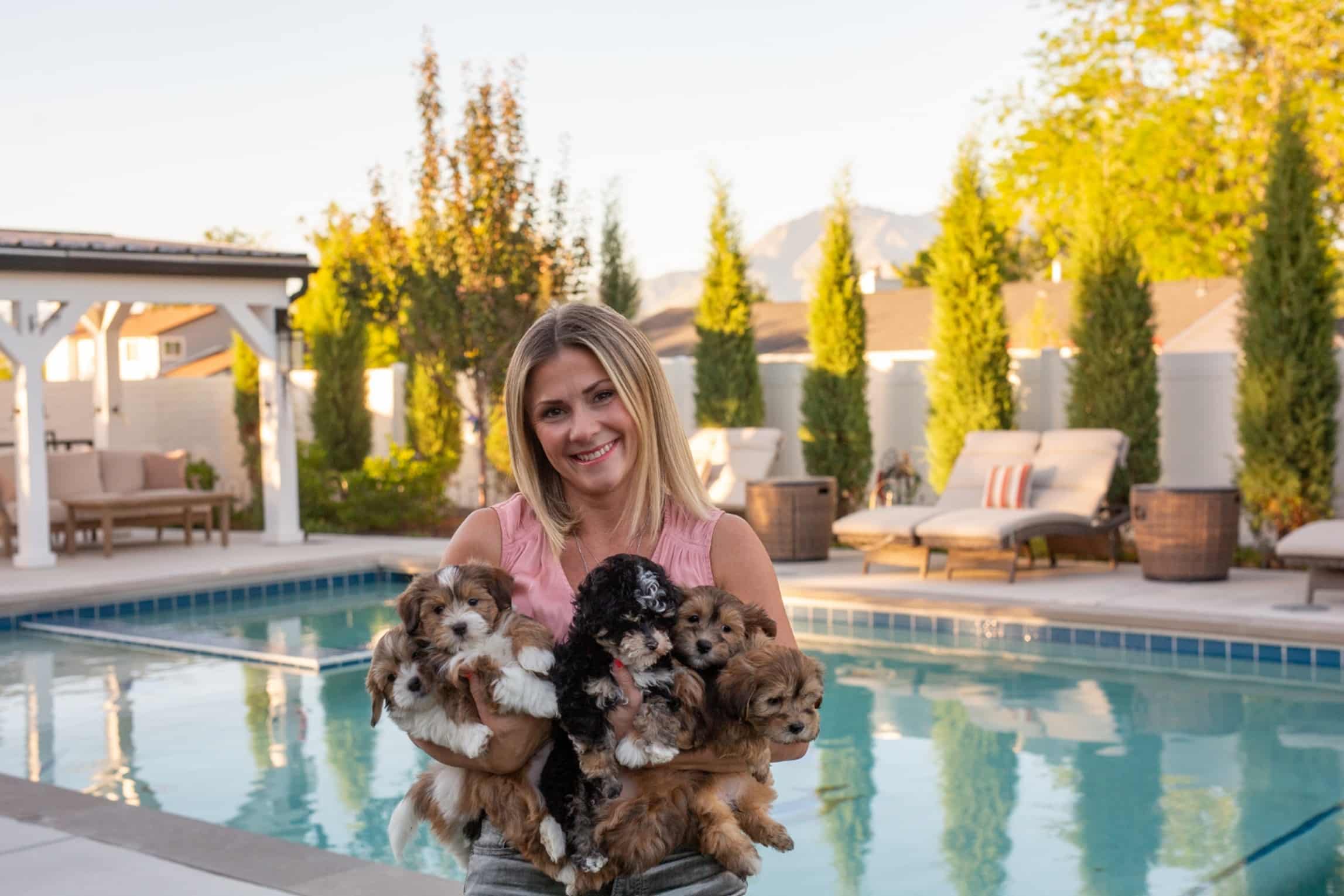 Woman holding several small puppies beside a backyard pool