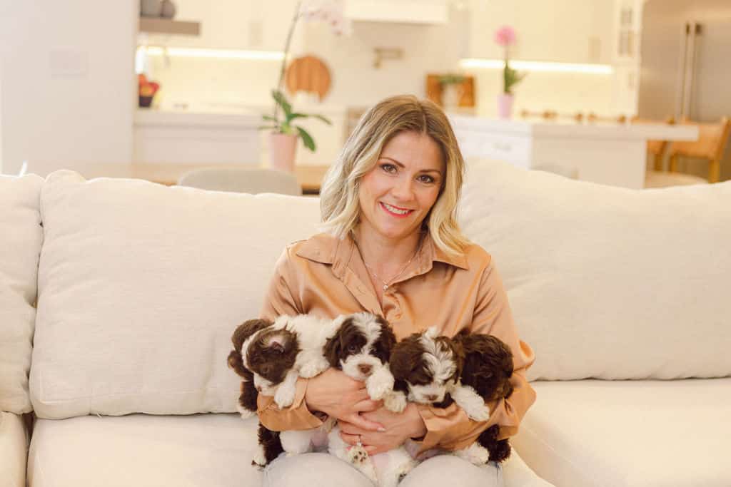 Woman sitting on a cream sofa while holding several small puppies