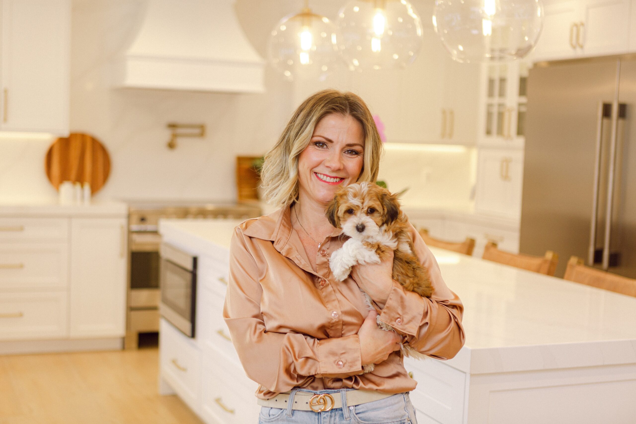 Woman holding an apricot and white puppy in a bright home kitchen