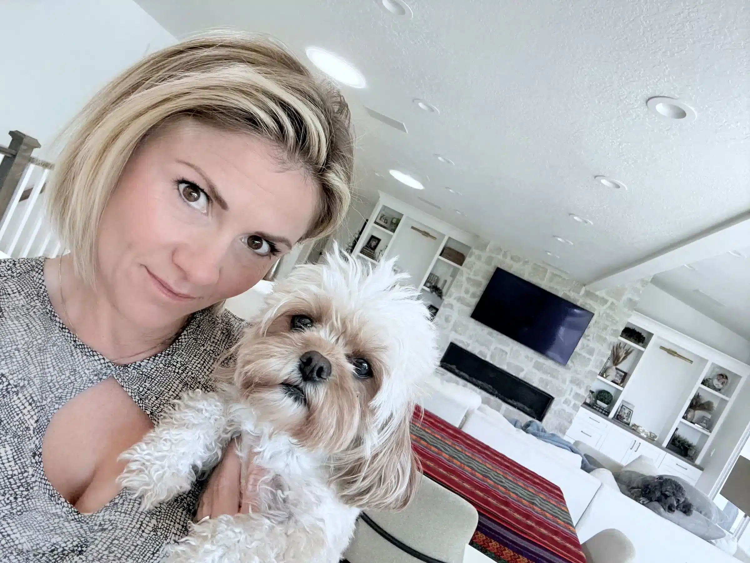 Woman With Small Dog | New York Sage Puppies Guide Woman holding a fluffy white-and-tan dog in a bright living room, pictured in a New York family guide