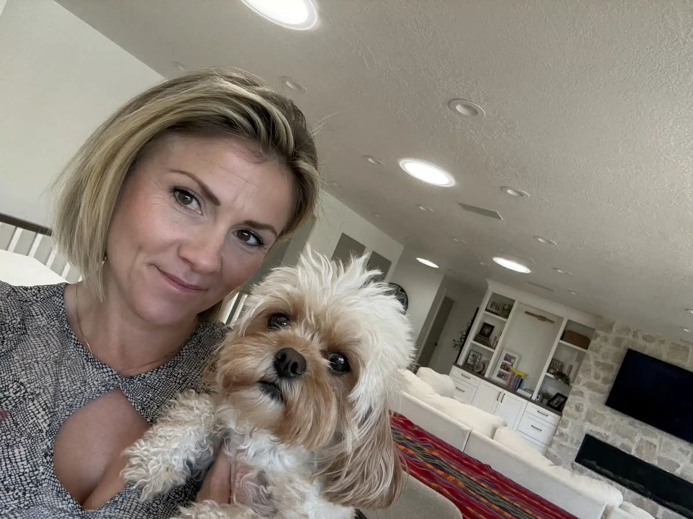 Woman beside a small cream-colored dog in a bright home.
