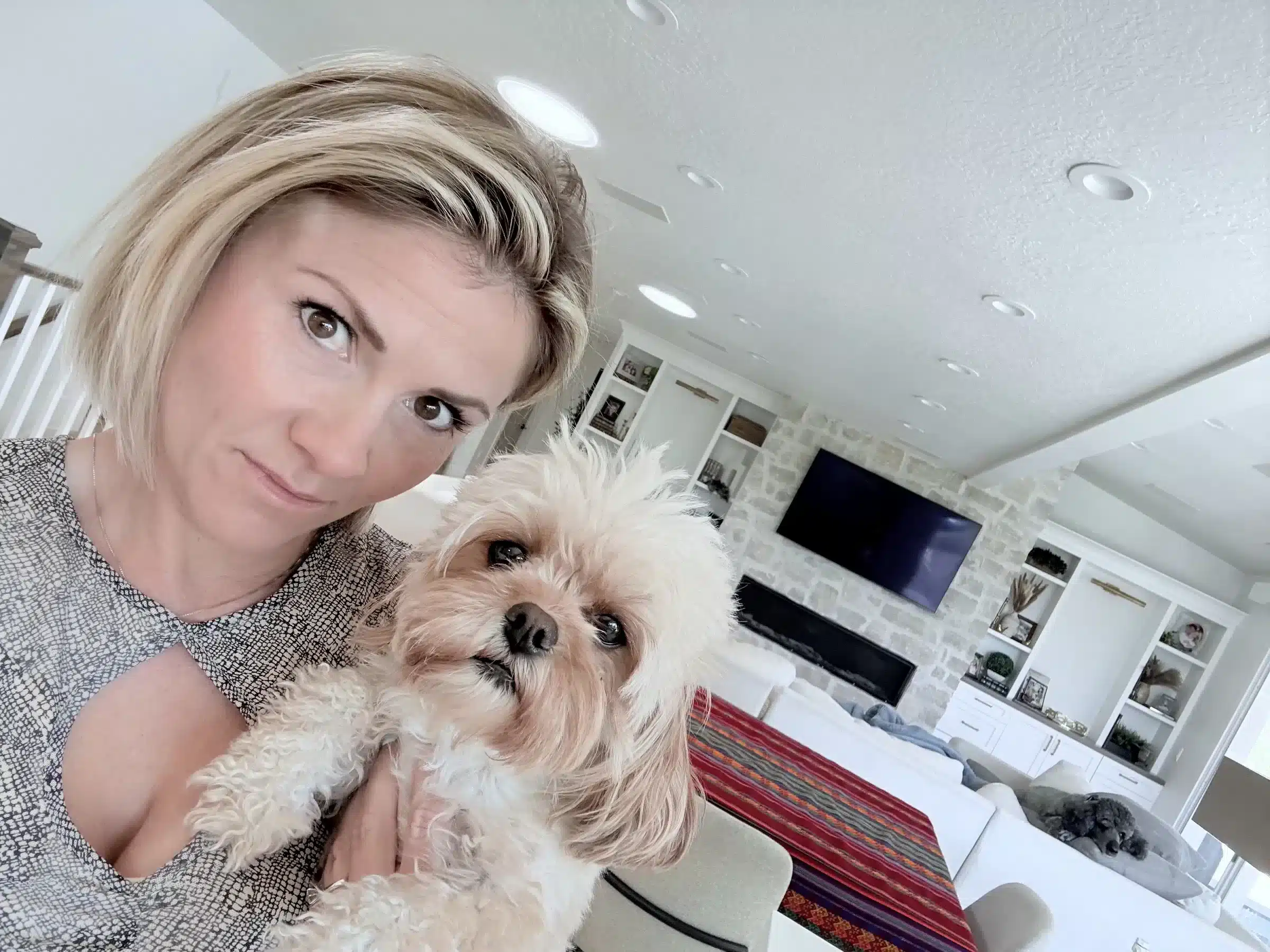 Woman holding a small cream dog with tan ears in a bright living room